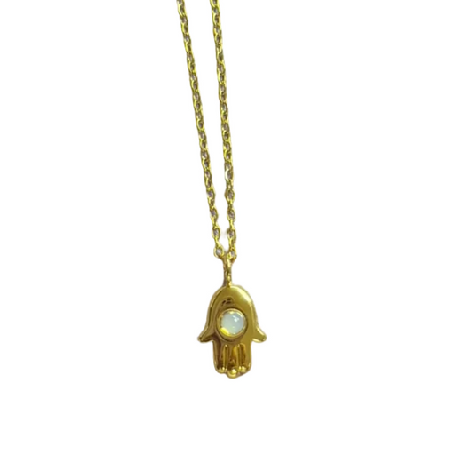 A gold hamsa hand pendant necklace with a small white inlay, shown on a light gray surface with a pink measuring ruler at the bottom for scale.